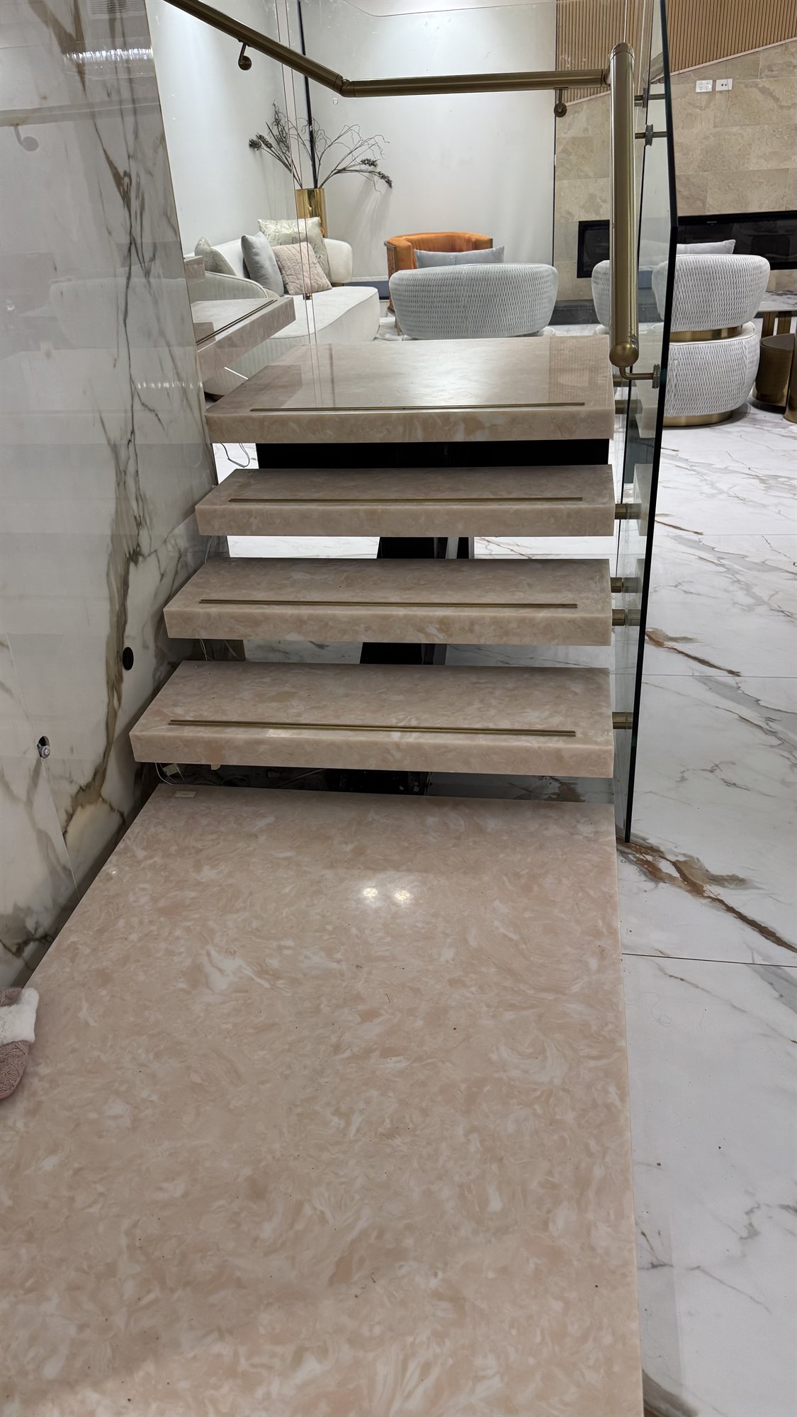 An existing pale marble floating staircase with a frameless glass balustrade and brass handrail in a finished Sydney home