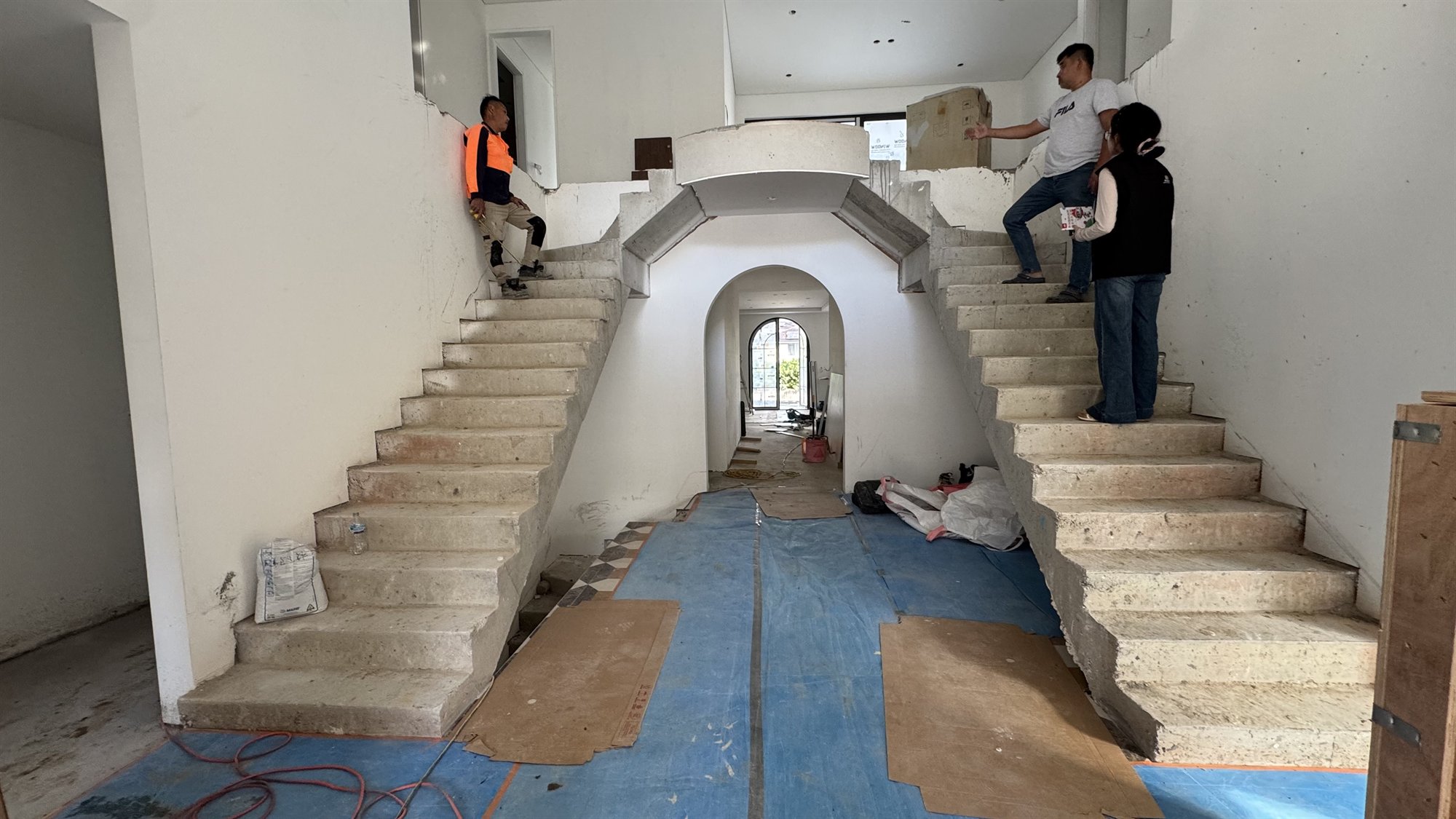 Twin poured-concrete staircases under construction in a Sydney home, flanking a central arched opening, before cladding