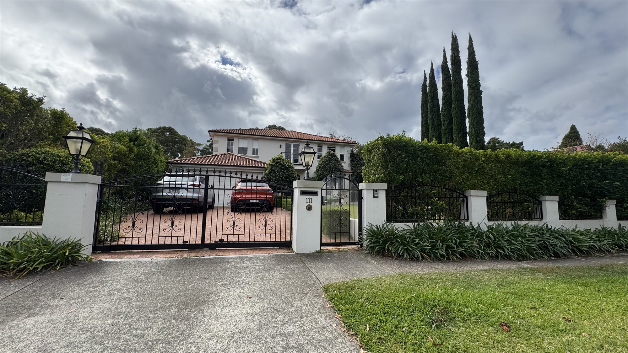 A leafy Sydney street with a grand Mediterranean-style home behind gates, in the kind of suburb these projects sit in