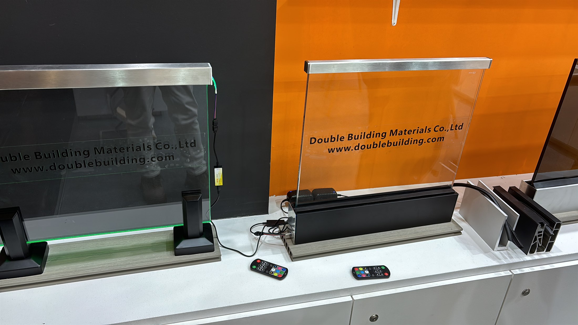 Two glass railing samples on a counter at BAU 2025, each set in a stainless base channel with colour-changing LED light and a handheld remote