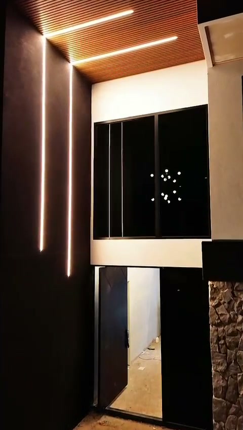 Black-framed aluminium glazing and entry lit from inside at night, with the stone feature wall, Adelaide new-build home