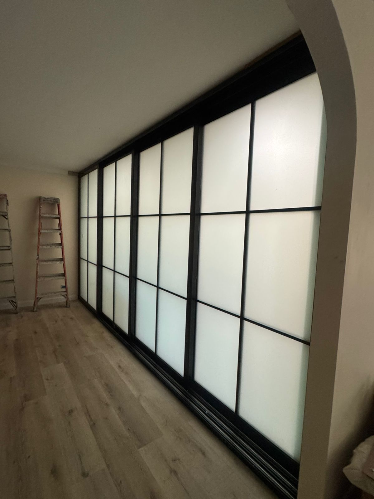 Black-framed frosted-glass sliding partition closing off a room under an arched opening, during fit-out of a home in Trinidad and Tobago