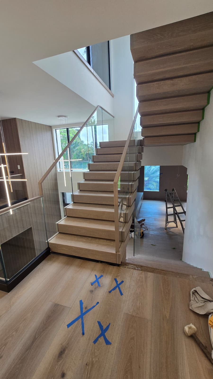 Finished white-oak switchback floating staircase turning at a half-landing, with a frameless glass balustrade and oak handrail, Florida home