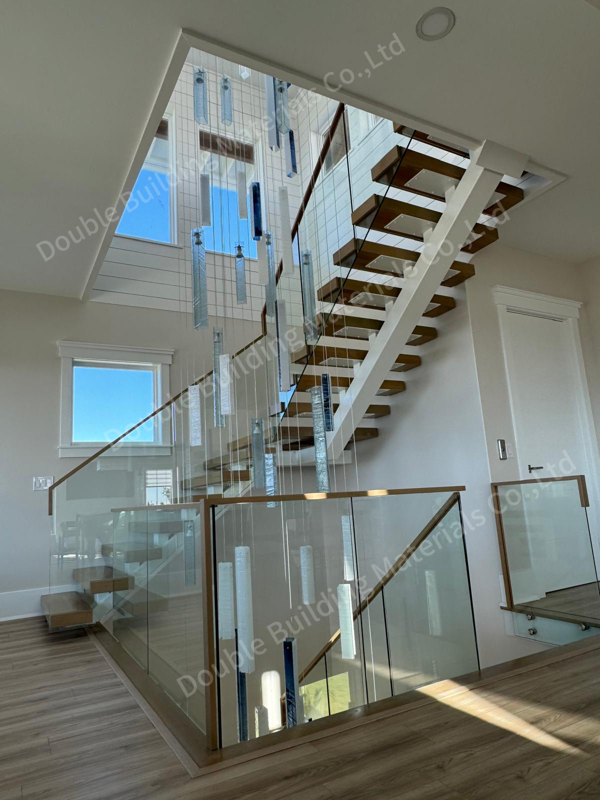 Square-tube floating staircase with light oak treads and a frameless glass railing rising through a tall window-lit void in a Virginia home