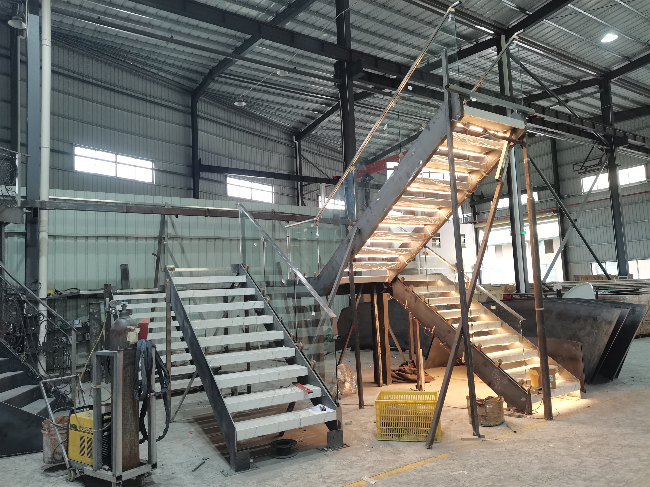 Trial assembly of the stone staircase and frameless glass railing flights side by side on the DBM workshop floor before crating