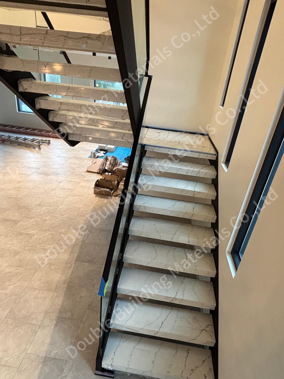 Stone-tread staircase on dark steel side panels with a frameless glass railing, during fit-out of a high-end home in Texas, United States