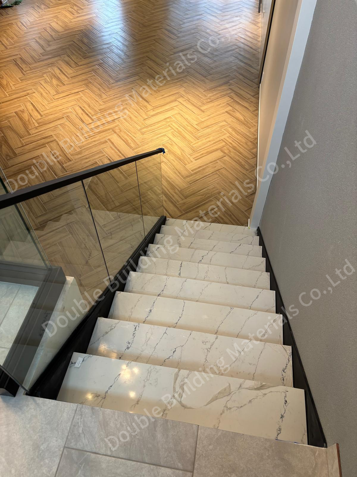 Looking down a stone-tread flight to a herringbone wood floor, with a frameless glass railing on a slim channel base, Texas home